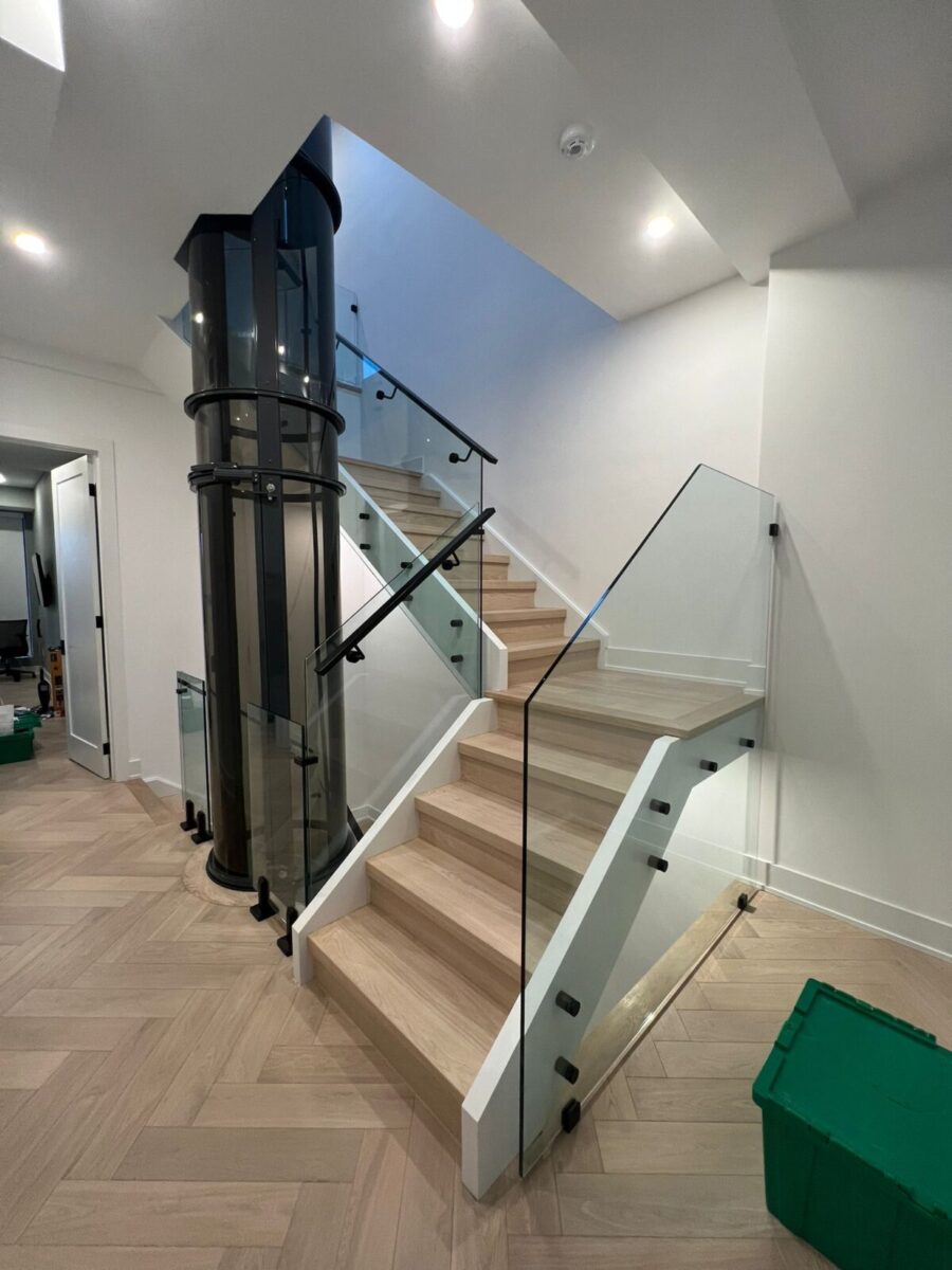 Modern interior frameless glass railing with 12mm tempered glass and a glass tube elevator inside a luxury Toronto home.