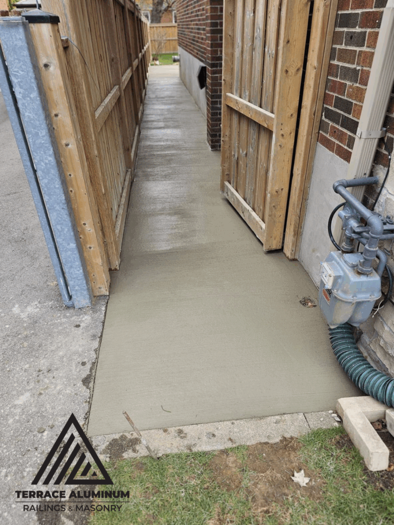 Newly poured concrete walkway installation beside house in Toronto – Terrace Aluminum Railings & Masonry.