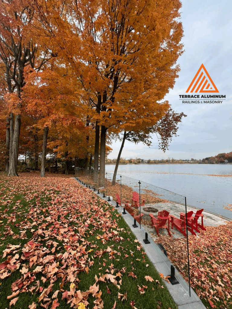 alt="Frameless glass railing on a retaining wall surrounded by fall leaves in Toronto, installed by Terrace Aluminum Railings with 12mm tempered glass panels for a clean modern design."