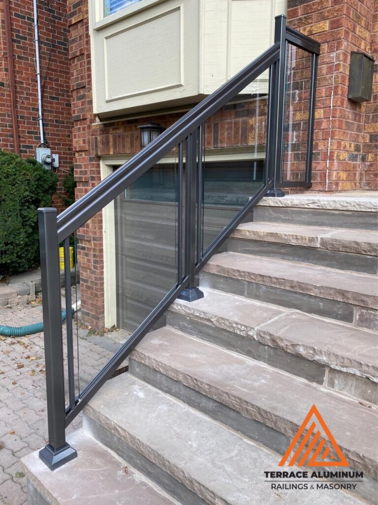 alt="Aluminum and glass railing on a flagstone porch in Toronto installed by Terrace Aluminum Railings, featuring clear tempered glass panels and black aluminum posts for a durable modern finish."