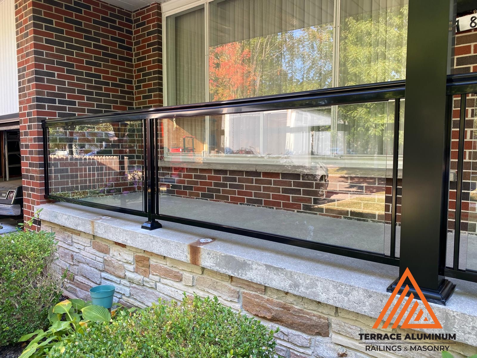alt="Aluminum glass railing installation on a Toronto front porch by Terrace Aluminum Railings, featuring clear tempered glass panels and black aluminum posts for a clean modern look."