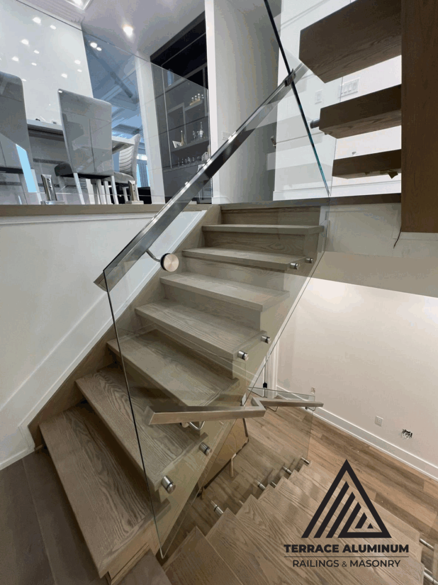alt="Interior frameless glass railing in Toronto installed by Terrace Aluminum Railings, featuring 12mm clear tempered glass panels and stainless steel fittings for a sleek open staircase design."