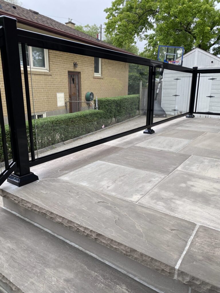 Black aluminum and glass railing installed on a flagstone front porch in Oakville by Terrace Aluminum Railings & Masonry. Modern aluminum frame with clear tempered glass panels for a clean, elegant finish.