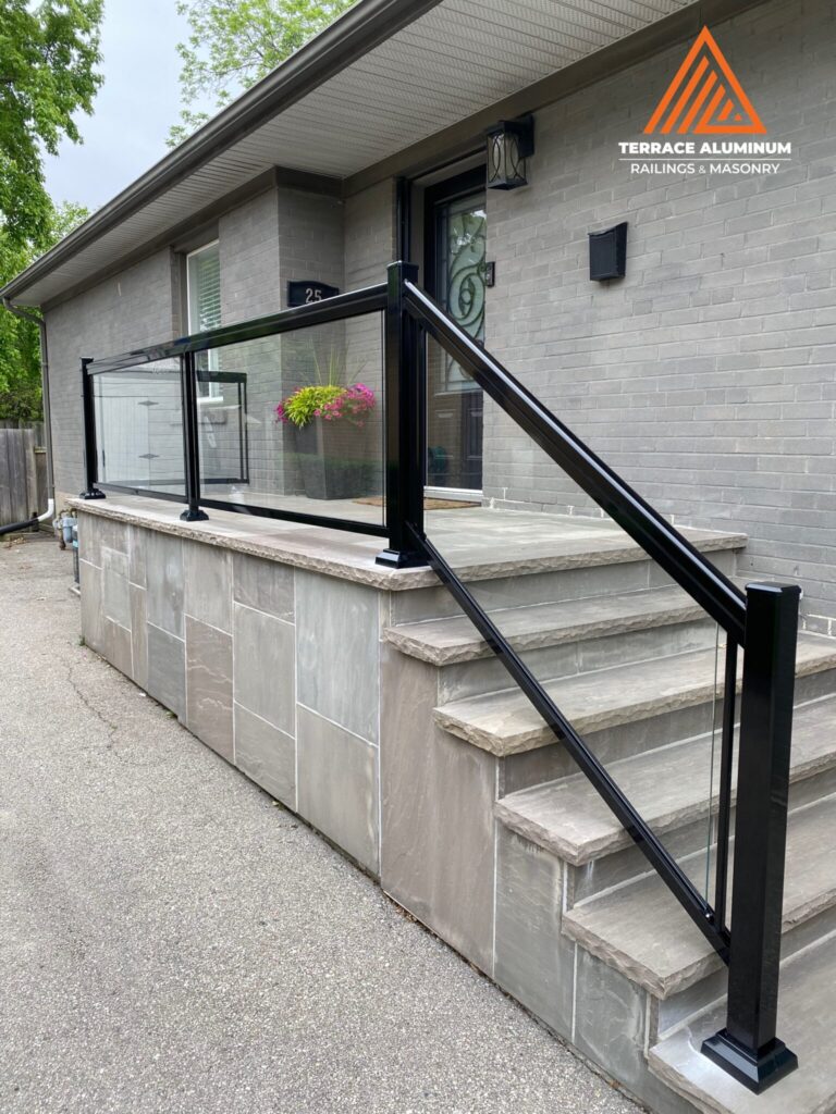 Framed aluminum and glass railing installed on a flagstone porch in Oakville with clear tempered glass panels.