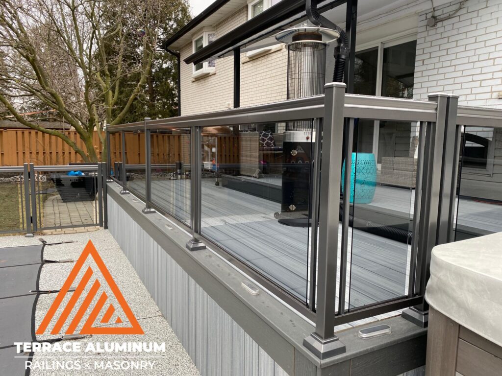 Bronze aluminum and glass railing installed on a backyard deck in Oakville by Terrace Aluminum Railings & Masonry. Tinted tempered glass panels framed in bronze aluminum for a modern and elegant outdoor design.