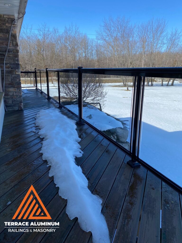 Glass railing on a deck in Oakville during winter snow, featuring clear tempered glass and aluminum posts.