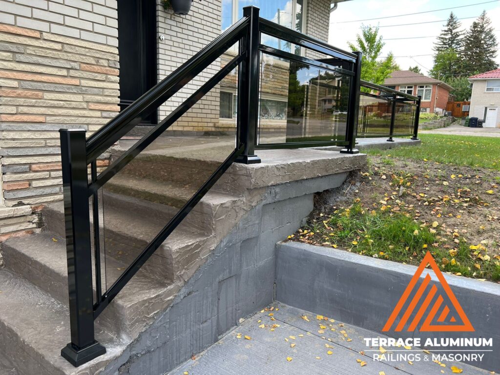 Are glass railings worth it? Framed aluminum railing with bronze tempered glass panels on a front porch offering warmth and privacy
