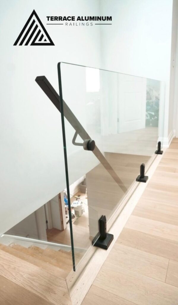 Interior frameless glass stair railing in Oakville installed by Terrace Aluminum Railings & Masonry. 12mm tempered glass with black standoff brackets for a clean, modern design on wood stairs.