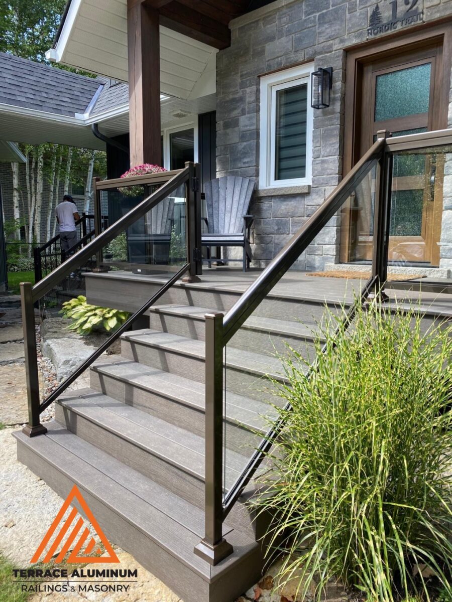 Aluminum and glass railing on front porch steps of a stone home in Oakville, installed by Terrace Aluminum Railings & Masonry. Clear tempered glass panels with brown aluminum framing for a warm, modern look.